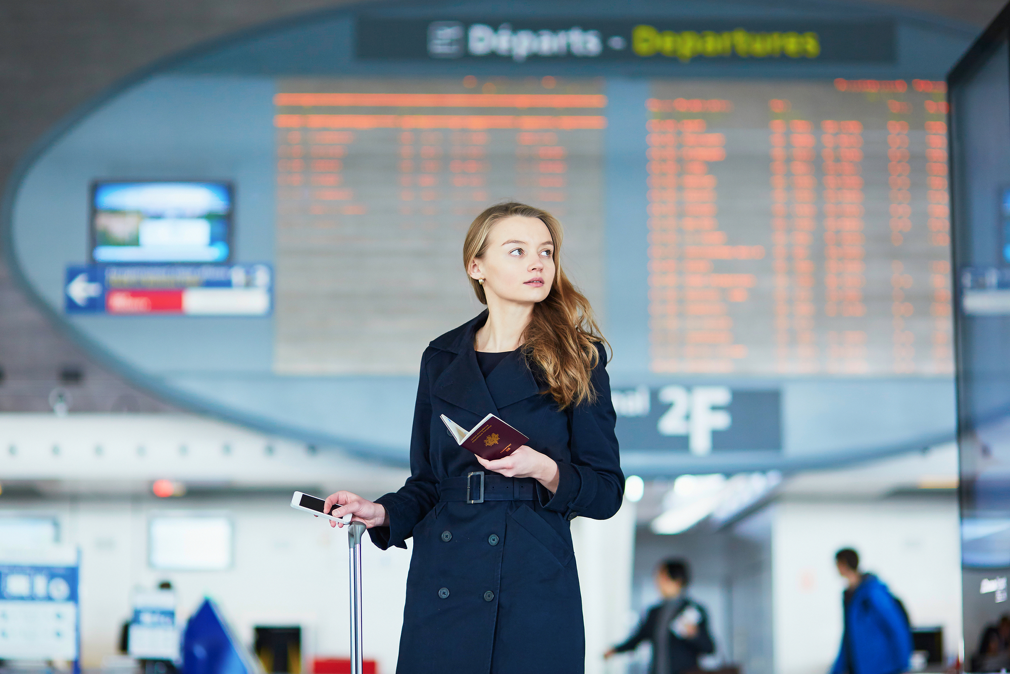 Young woman in international airport near the flight information board, holding French passport in her hand